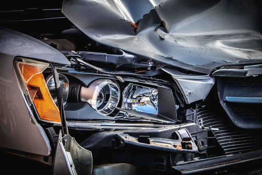 Ilustrasi mimpi kecelakaan mobil — A damaged silver car with a crushed hood and broken headlight assembly