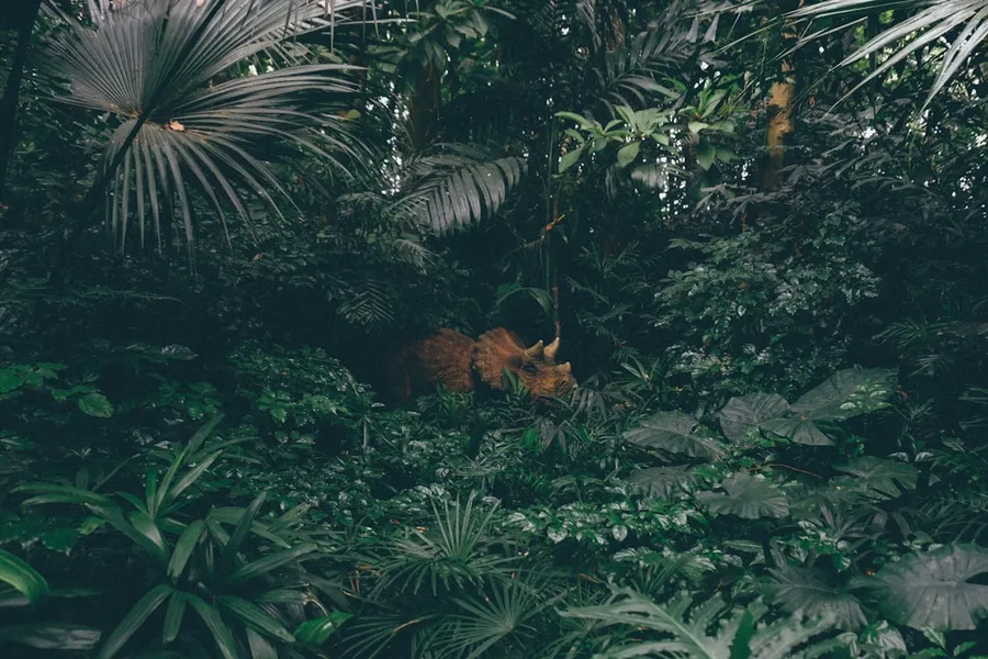 Ilustrasi mimpi tembak macan — brown triceratops surrounded by plants